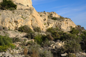 Rugged rocky hillside terrain with sparse vegetation and clear blue sky