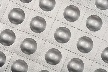 A close-up, top-down view of multiple rows of silver blister packs with round indentations for...