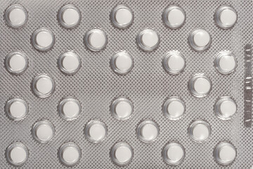 A close-up shot of a blister pack filled with small, round, white pills, neatly arranged in a silver foil packaging