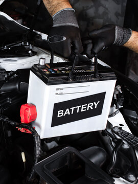 Car battery replacement , Automotive repair concept.  Hands installing a car battery in a vehicle engine bay. Indoor shot of garage.