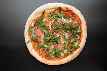 Delicious pizza topped with fresh arugula, salami, and ham on a black background