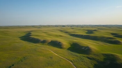 An expansive green grassland with gentle rolling hills and blue sky