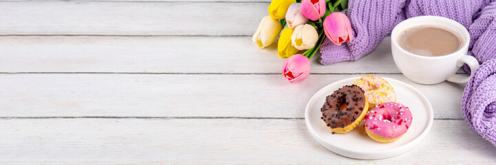 Small sugar glazed donuts with coffee latte cup, tulip flowers, sweater, tulip flower bouquet and note Good Morning. Spring holiday, Mother Day, Woman day, Birthday greeting card background 