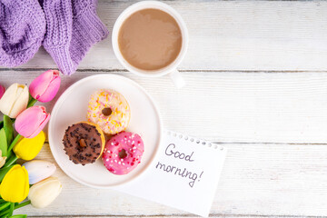 Small sugar glazed donuts with coffee latte cup, tulip flowers, sweater, tulip flower bouquet and note Good Morning. Spring holiday, Mother Day, Woman day, Birthday greeting card background 