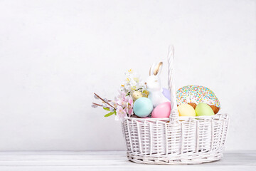 Traditional Easter basket with Easter cake, colorful pastel colored eggs, bunny rabbits decor and spring flowers. Preparation for Easter celebration, greeting card, invitation, Easter sale background
