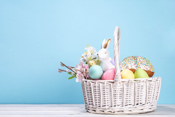 Traditional Easter basket with Easter cake, colorful pastel colored eggs, bunny rabbits decor and spring flowers. Preparation for Easter celebration, greeting card, invitation, Easter sale background
