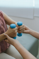 Senior woman exercising with dumbbells during physical therapy in hospital. Physiotherapist helps...