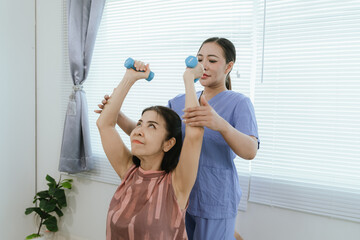 Senior woman exercising with dumbbells during physical therapy in hospital. Physiotherapist helps...