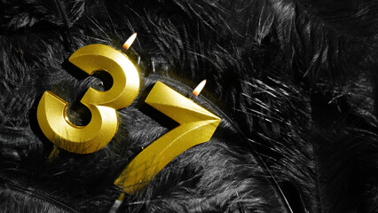 Number 37 golden celebration birthday candle on Black Feathers Background. Thirty-seventh year....