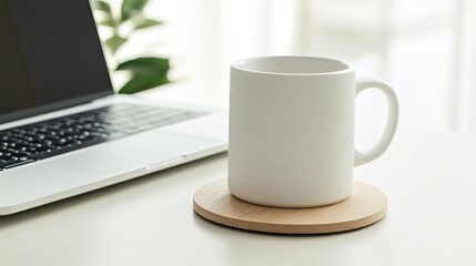 A mug on a wooden coaster and a computer on a table create a light-colored, serene and minimalist workspace. Harmony is created between simplicity and modernity.
