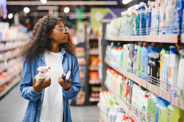A african american young woman chooses household chemicals in a supermarket. Means for washing and cleaning the house
