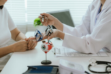 Asian female doctor talking to elderly patient, showing eye model and explaining about eye disease...