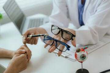Asian female doctor talking to elderly patient, showing eye model and explaining about eye disease...