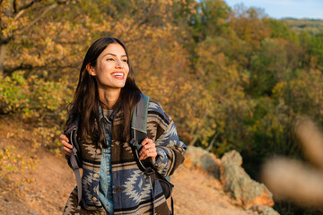 Young woman hiking along a vibrant trail in an autumn forest, smiling joyfully amidst the colorful...