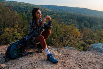 Female hiker sitting on a rock, eating energy bar while enjoying the view of a valley during a hike