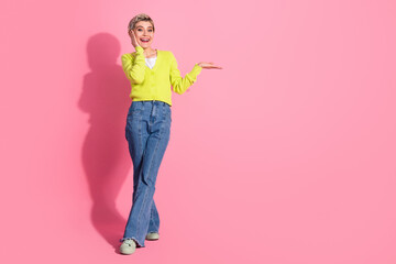 Cheerful young woman in a yellow cardigan and jeans, gesturing with her hand on a vibrant pink background promoting mood