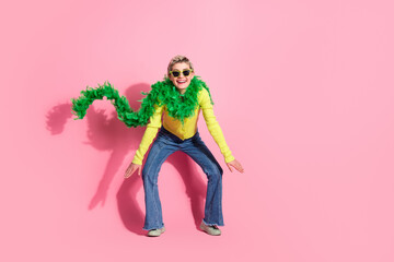 Young fashionable woman wearing a green boa and sunglasses posing playfully against a vibrant pink background