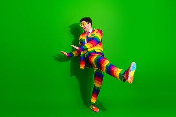 Vibrant young man posing in a colorful rainbow suit, standing against a green background