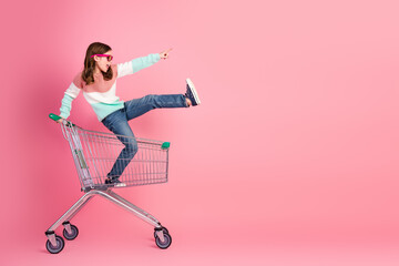 Young pretty girl in a shopping cart expressing joy with a bright pink background, showcasing...