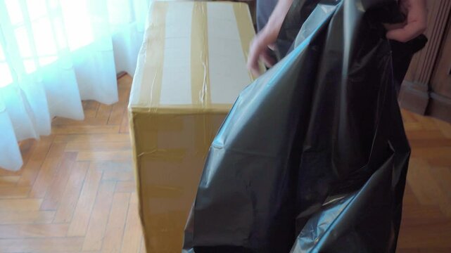Man wrapping cardboard box in black plastic bag