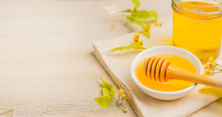 Honey bee in glass jar and bowl with linden flower with honey dipper on wooden background.