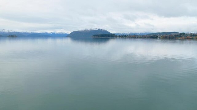 Aerial footage of Lake Wānaka in Otago, New Zealand, featuring the iconic That Wānaka Tree surrounded by autumn foliage and calm turquoise waters. Captured by drone, the scenic landscape highlights