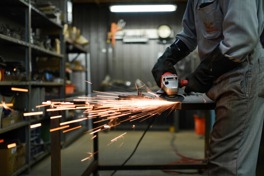 Male worker using angle grinder in workshop with safety gear and sparks flying