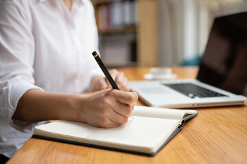 Female writing notes at wooden desk with laptop in office environment