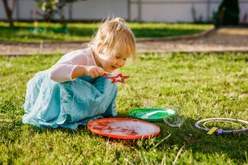 Little girl in princess dress blowing soap bubbles in a sunny garden during outdoor playtime