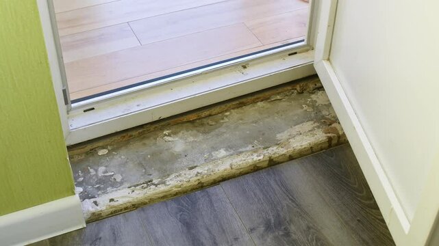 Unfinished door threshold with exposed subflooring in home renovation scene, highlighting incomplete repairs and raw edges.