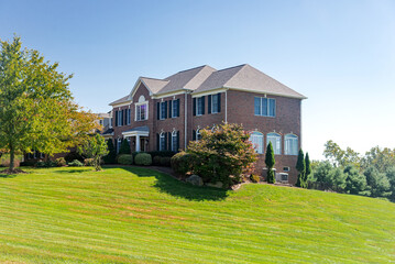 Large brick house with a green lawn side view. Landscape on a summer sunny day.