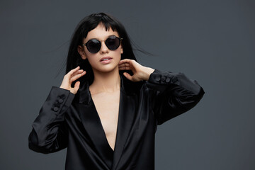 Asian woman wearing sunglasses and a black blazer stands confidently against a gray background,...