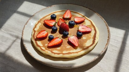 Freshly made pancakes served with sweet strawberries and blueberries for breakfast or brunch