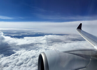 Aerial view of sky and clouds from above seen through the aircraft window, travelling by plane, magnificent breathtaking view during flight high through the cumulus clouds