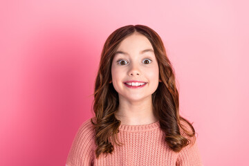 Smiling pretty girl with wavy brown hair in a casual pink sweater posing enthusiastically against a...