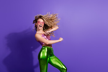 Happy young woman in shiny outfit dances against vibrant purple background, exuding fun and energy
