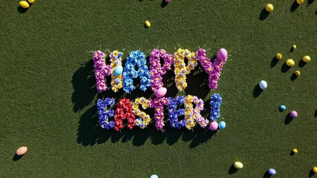 Aerial view of 'Happy Easter!' spelled with colorful flowers on grass, surrounded by eggs. Bright, festive style perfect for a holiday video theme.