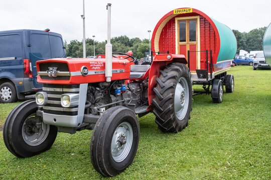 Ballymena, Northern Ireland - July 20th, 2024: vintage tractor and steam engine rally, red classic Massey Ferguson with retro style caravan on trailer. 