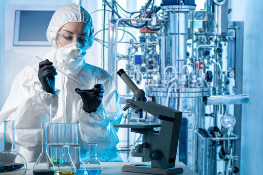 Laboratory assistant with microscope bio tech. Biologist at work. Scientist near bioreactor. Biologist in protective suit. Laboratory assistant makes scientific experiment. Biologist with flask