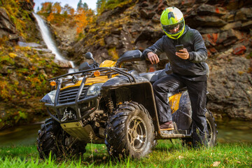 Man on quad bike. Guy on ATV in mountains. Off-road driving. Quad biker loves extreme sports. Male ATV driver. Extreme man looks away. Dangerous sports with ATV. Quad bike driver under blue sky