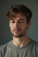 Obraz premium Focused Young Man with Tousled Hair Wearing Wireless Earbuds, Concentrating or Listening to Music, Ideal for Technology and Lifestyle Content