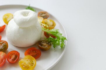 Buratta on a gray plate with cherry tomatoes and herbs on a white table. Traditional Italian food concept. Horizontal orientation. Selective focus. Copy space