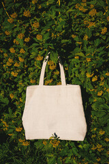 White canvas tote bag mockup template with long handles among the green plant leaves outdoor
