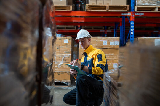 Man warehouse worker wearing uniform and helmet safety with clipboard for checking stock products on shelves in warehouse. Logistics, Distribution Center concept
