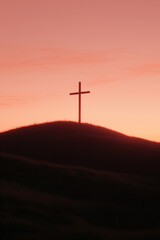 Silhouette of a cross on a grassy hill against a colorful sky at dusk, symbolizing faith and hope.