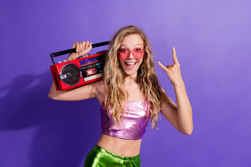 Joyful young woman with a boombox on a purple background, feeling the retro vibes in a stylish and...
