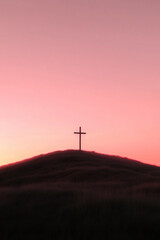 Obraz premium Hilltop Silhouette: Serene cross on a hill against a soft pink sky at dusk, symbolizing hope and faith.