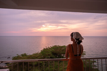 Beautiful Thai woman enjoys the view from the balcony of a beach resort during sunset. Beautiful tourist attraction on Koh Sichang, Chonburi Province, Thailand.