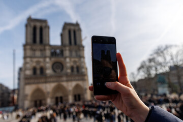 Naklejka premium A person is holding a cell phone up to take a picture of the Notre Dame cathedral