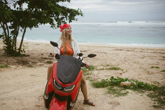 Attractive caucasian woman in a bikini swimsuit and on a bike scooter near the beach in sunny weather.